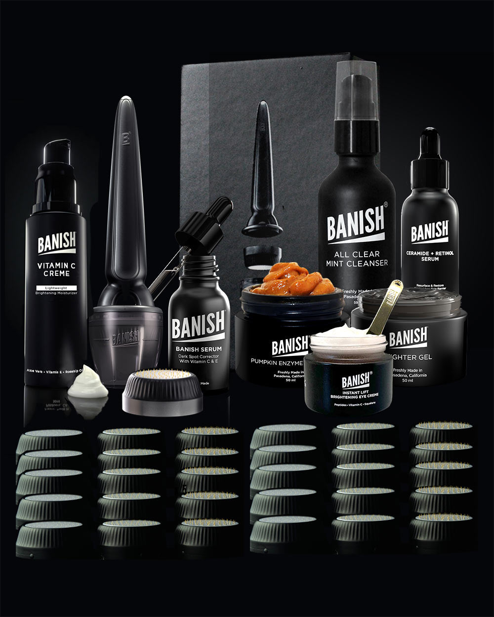 A collection of skincare and grooming products from BANISH, including a microneedling stamper,  a pumpkin enzyme mask, a fighter gel in a jar, multiple replacement heads for the banisher tool, vitamin c serum, and vitmain c creme on a black background.
